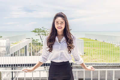 Portrait of smiling woman standing against railing and sky