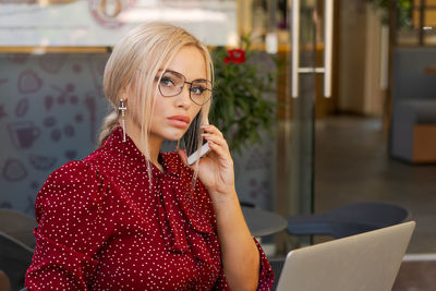 Beautiful woman works on laptop in coffee shop and using mobile phone in a red