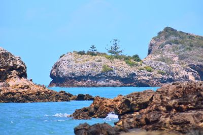 Rock formations in sea against clear blue sky