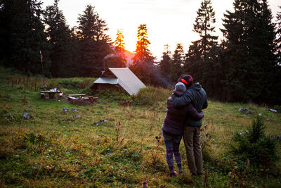 Rear view of couple standing on field against trees