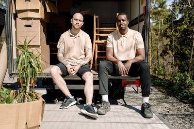 Portrait of multiracial movers sitting at trunk of delivery truck