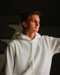 Portrait of young man looking away while sitting against black background