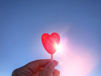 Cropped hand of person holding heart shape candy against sky