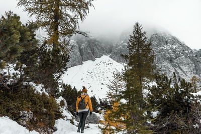 Rear view of female hiker walking on snowy path in misty mountains