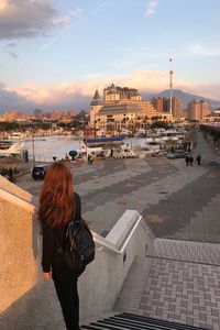 Rear view of woman with cityscape against sky during sunset