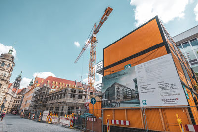 Low angle view of crane by buildings against sky