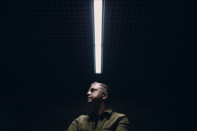 Portrait of young man looking away against black background