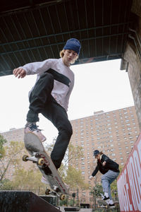 Low angle view of friends skateboarding against buildings in city