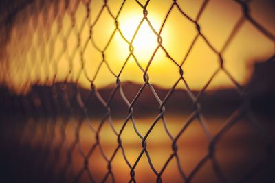 Close-up of chainlink fence against sunset sky