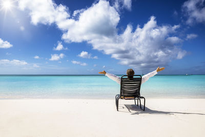 Rear view of woman sitting on beach against sky