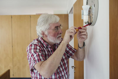 Senior man repairing sconce with screwdriver at home