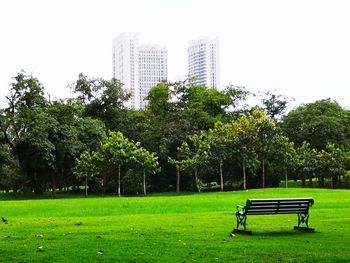 Park bench on field by trees against sky