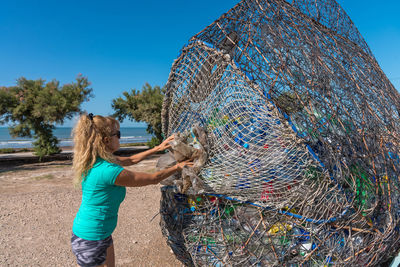 Mature woman putting a plastic into a very large trash can full of recyclable material.