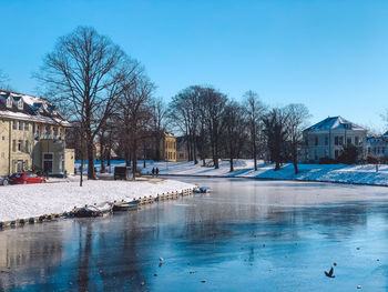 Scenic view of frozen river by building against blue sky