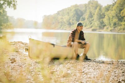 Mid adult man looking away while sitting on boat at lakeshore