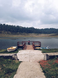 Woman standing on pier over lake against sky