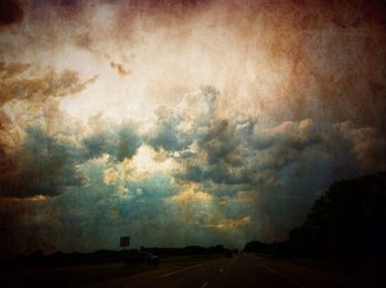 Road by silhouette landscape against storm clouds