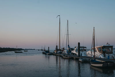 Sailboats moored in harbor at sunset