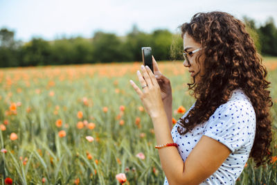 Side view of young woman using mobile phone on field