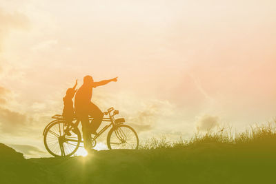 Man riding bicycle on field against sky during sunset