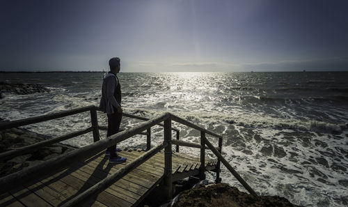 Side view of man standing on pier over sea