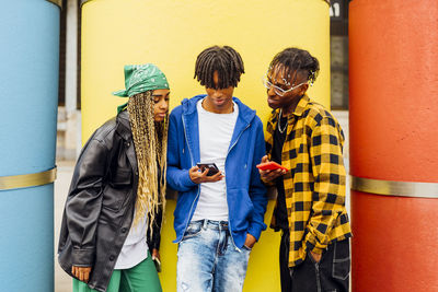 Young man sharing smart phone with friends in front of yellow pipe