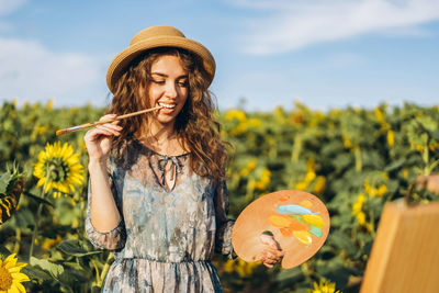 Woman wearing hat holding plants against sky