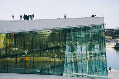 People on glass building in city against sky