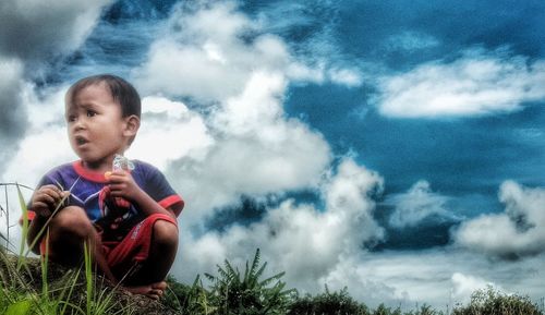 Low angle view of boy sitting against sky