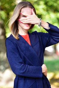 Portrait of woman looking covering eye while standing in park