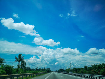 Road by trees against blue sky