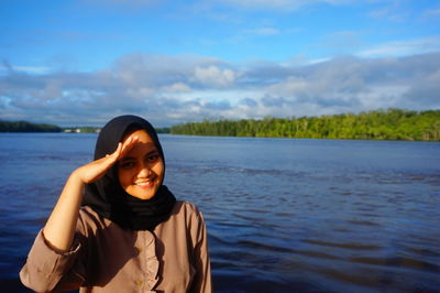 Portrait of smiling young woman standing against sky