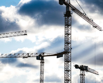 Low angle view of cranes at construction site against sky