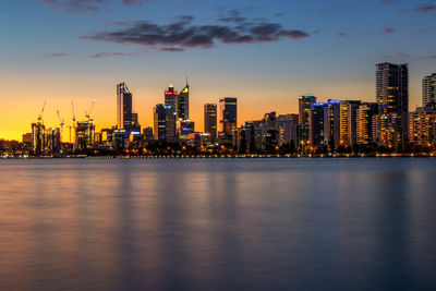 Sea by illuminated modern buildings in city against sky