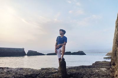 Man standing on rock by sea against sky