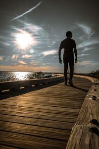 Rear view of man standing on pier over sea against sky during sunset