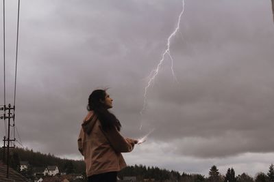 Side view of woman standing on field against lightning