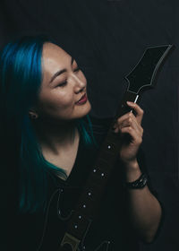 Woman holding guitar while standing against wall