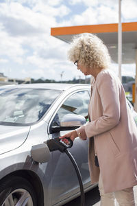 Side view of senior woman refueling car at gas station