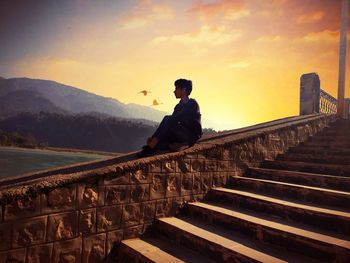 Side view of man sitting on staircase against sky