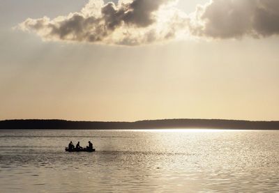 Silhouette fishermen sailing boat in lake against sky during sunset