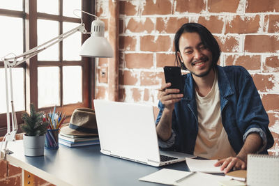 Smiling young woman using mobile phone while sitting on table