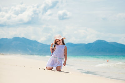 Cute girl kneeling on beach against sky