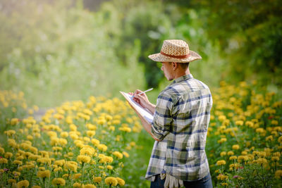 Man holding camera while standing by yellow flowers