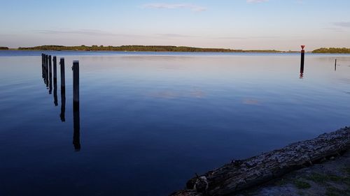 Wooden posts in lake against sky