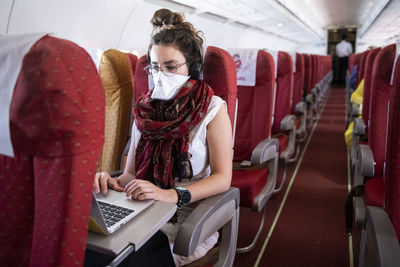 Young woman wearing a face mask while she works on an almost empty airplane due to the travel concerns and restrictions caused by the covid-19 pandemic.