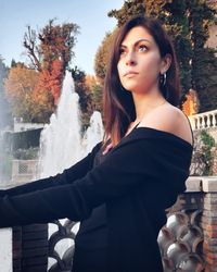 Portrait of beautiful young woman standing against trees