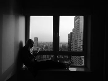 Side view of woman sitting on window sill