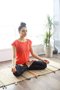 Full length of woman meditating while sitting on wooden floor