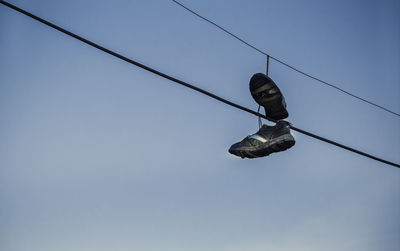 Low angle view of shoes hanging on cable against sky